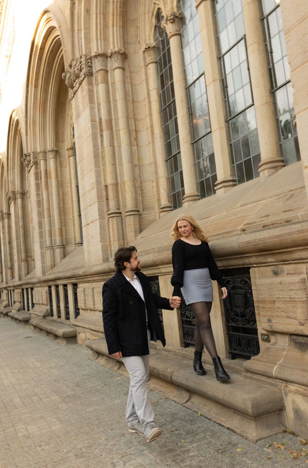 A couple interacts playfully on stone church steps during a photoshoot.