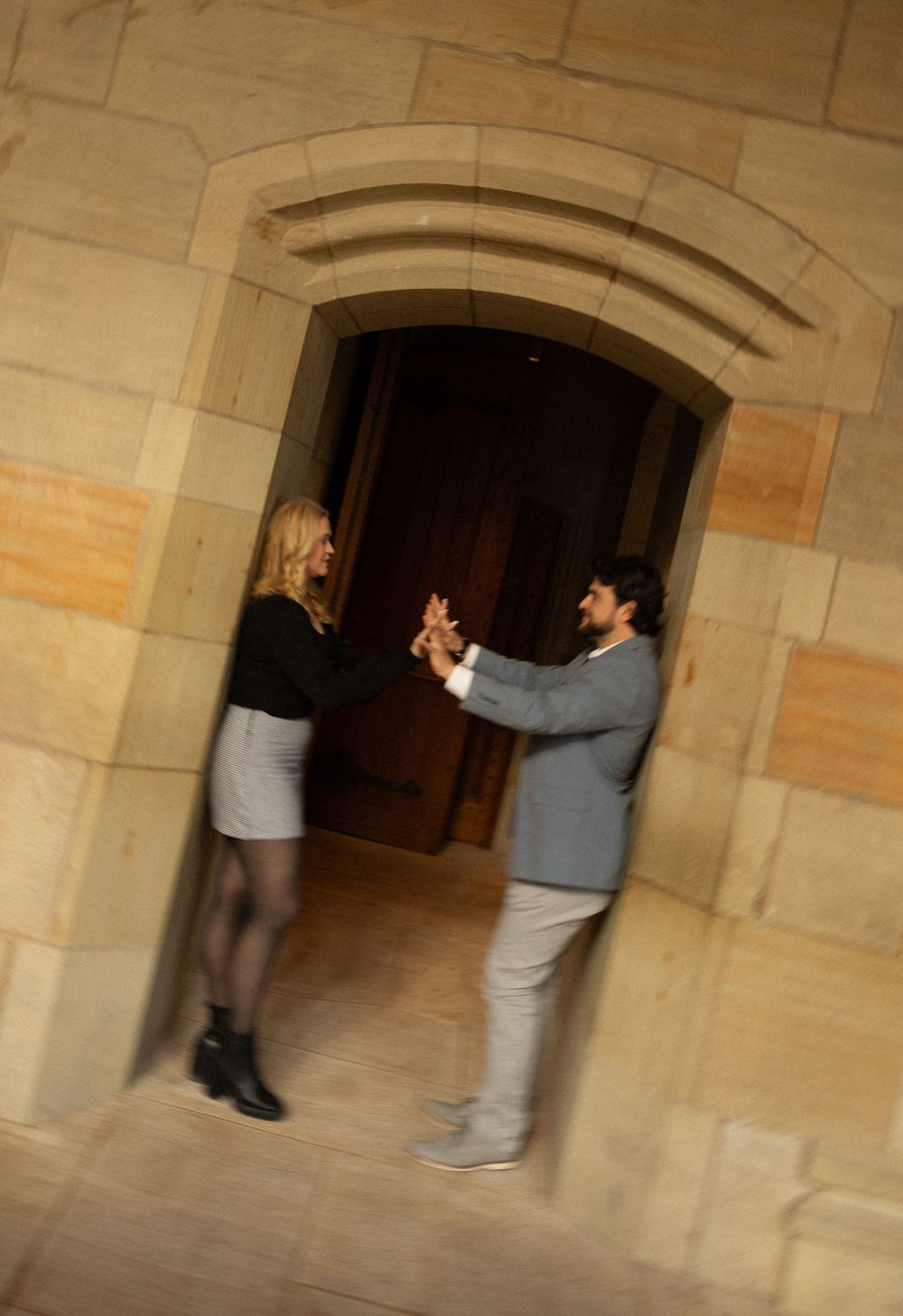 A couple interacts playfully in an arched stone doorway of a historic building.