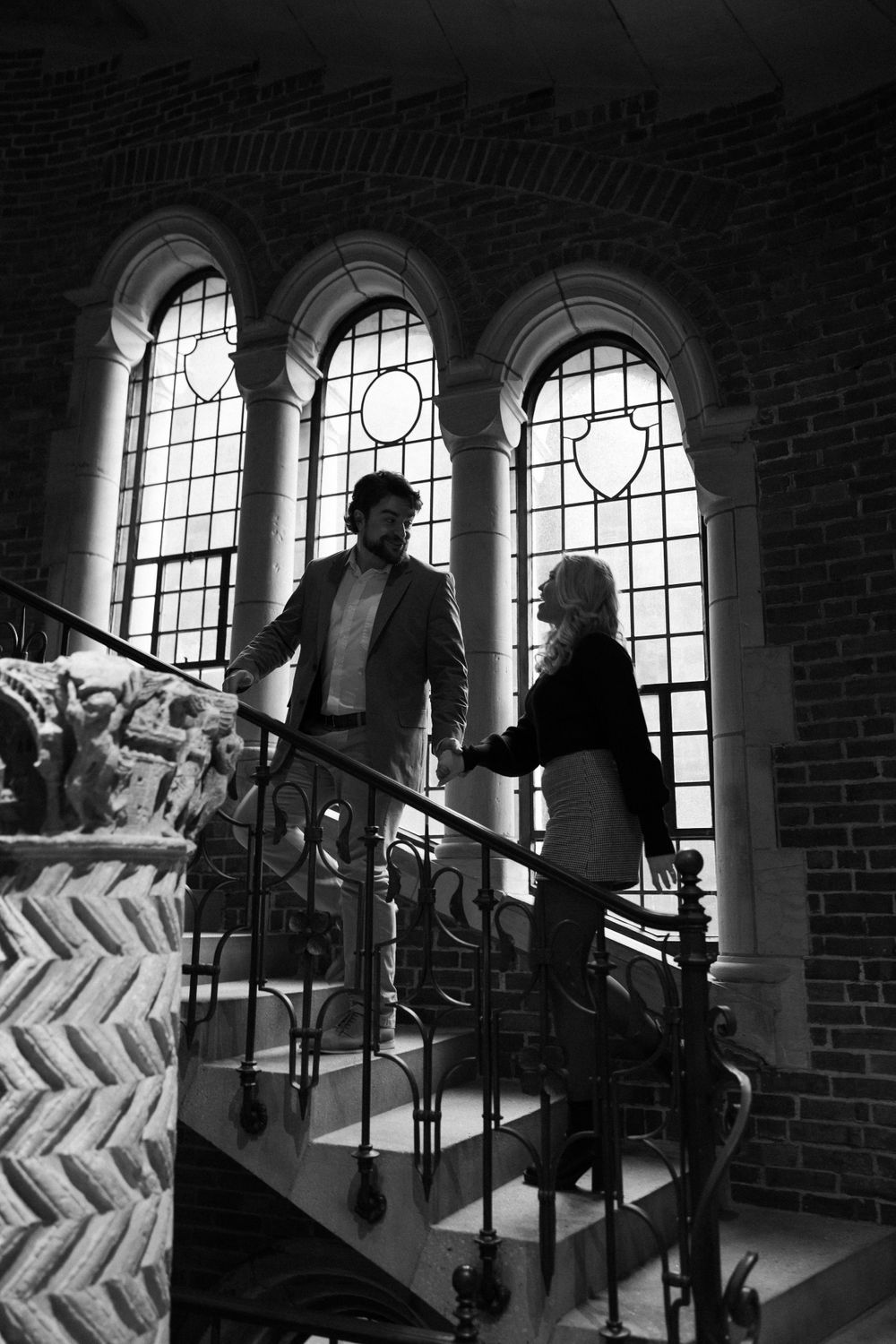 Silhouettes of two people on a gothic staircase with arched windows in black and white.