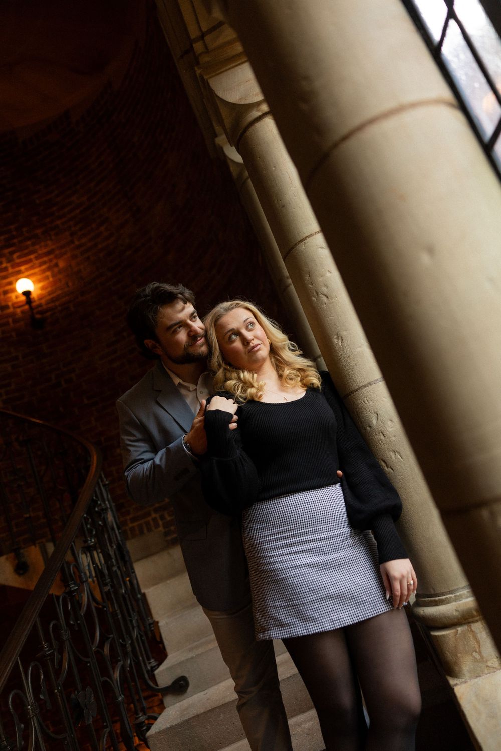 A romantic moment captured between two people near a stone column with warm lighting.