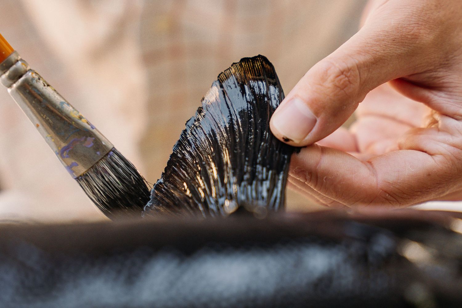 Hand holding paintbrush applying dark paint with precise brushstrokes.