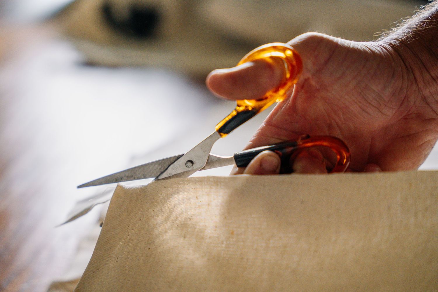 Hands using scissors to precisely cut through light colored material.