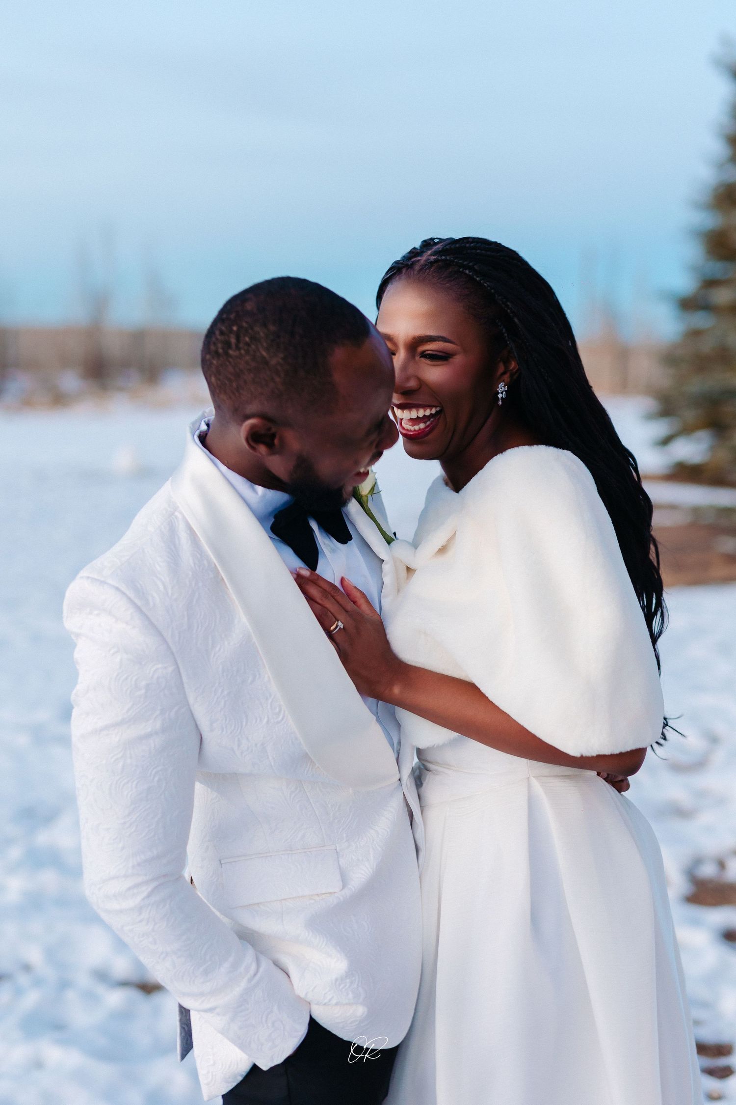 Romantic winter portrait of couple in white outfits laughing together in snowy setting.