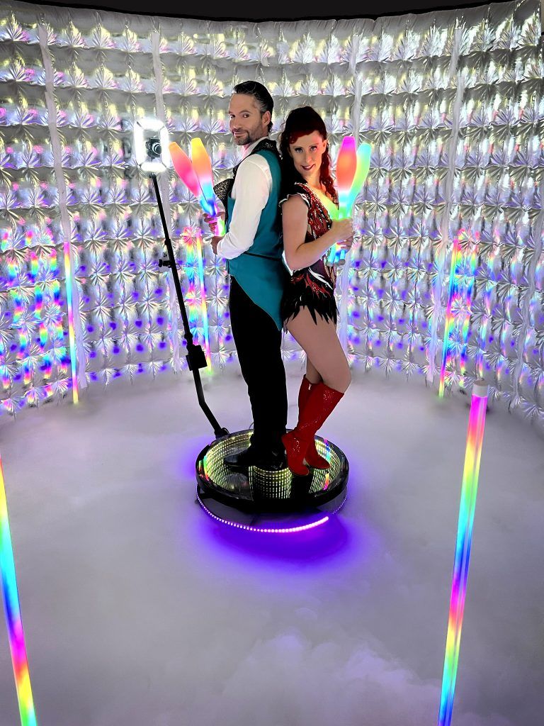 Event 360-degree photo booth rental platform with two guests posing under colorful LED lighting. 360 video booth vivitu kevelaer