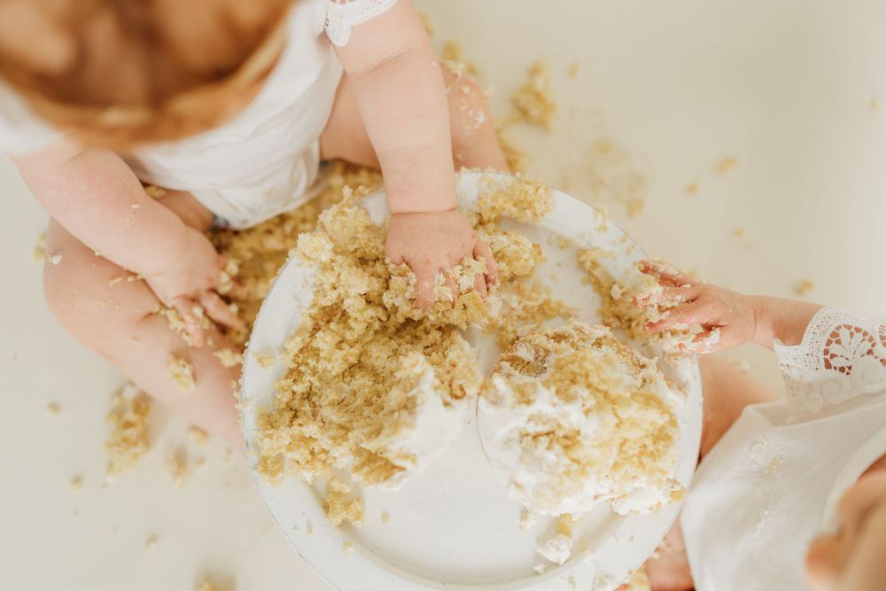 Small hands playing in cake crumbs and frosting during a cake smash photo session.