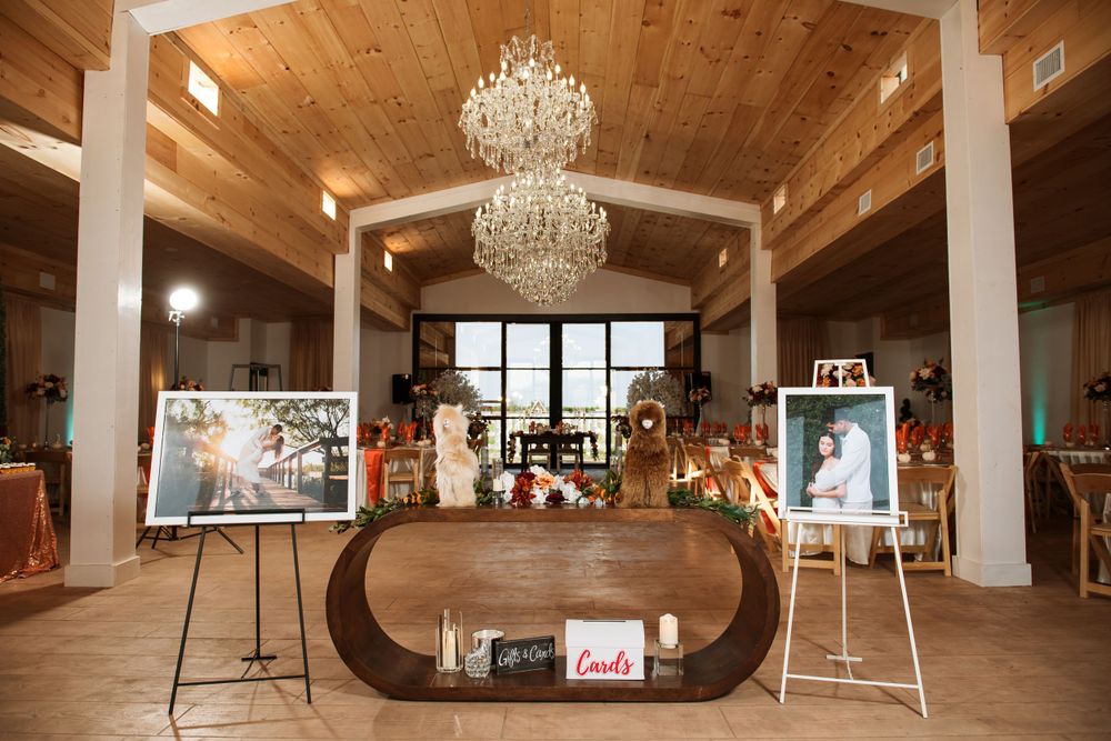 Elegant wedding venue interior with wooden ceiling, crystal chandeliers, and display stands featuring framed photographs.