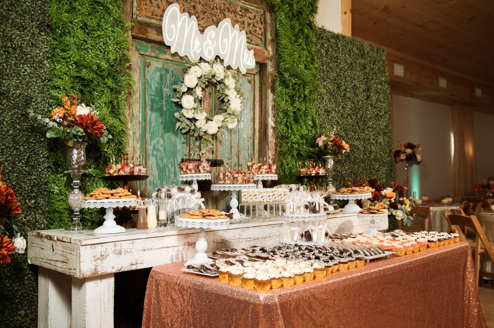 Luxurious dessert and appetizer table with greenery wall backdrop and elegant white serving stands.
