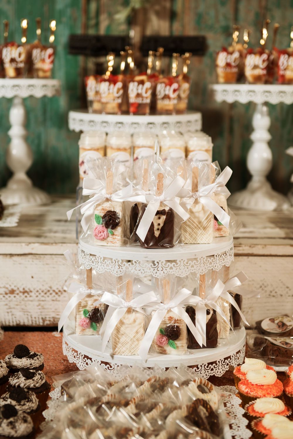 Wedding favors and treats displayed on ornate white tiered stands with decorative bows and ribbons.