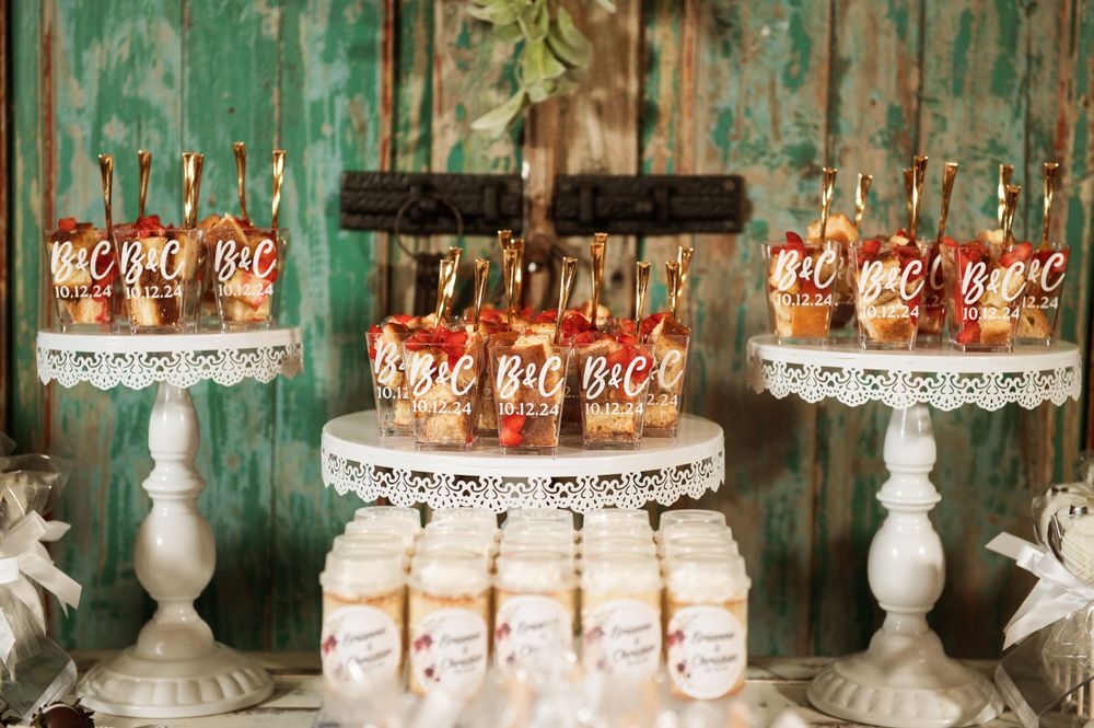 Vintage-style dessert display featuring bottled drinks and treats on white pedestal stands against weathered green wood.