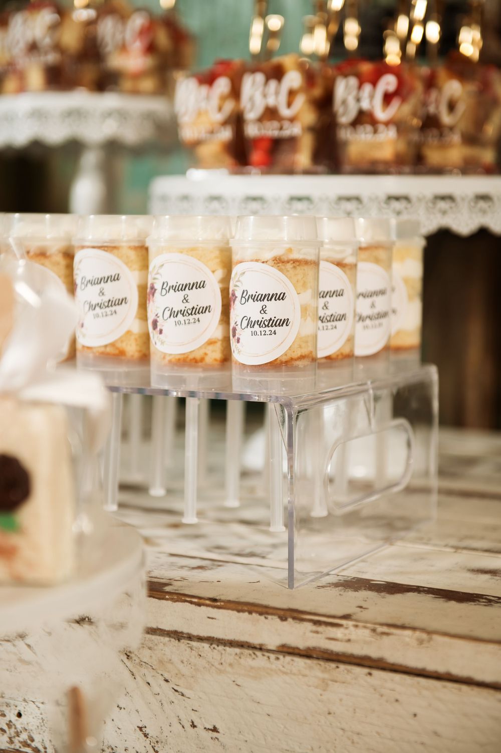 Wedding favor display with custom labeled bottles arranged on clear acrylic stands against distressed wood.