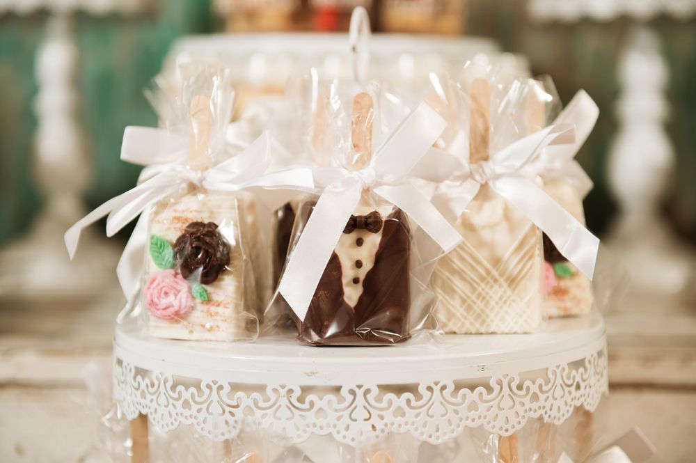 Close-up of wedding favors decorated with white bows and bride and groom designs on a lace-trimmed stand.