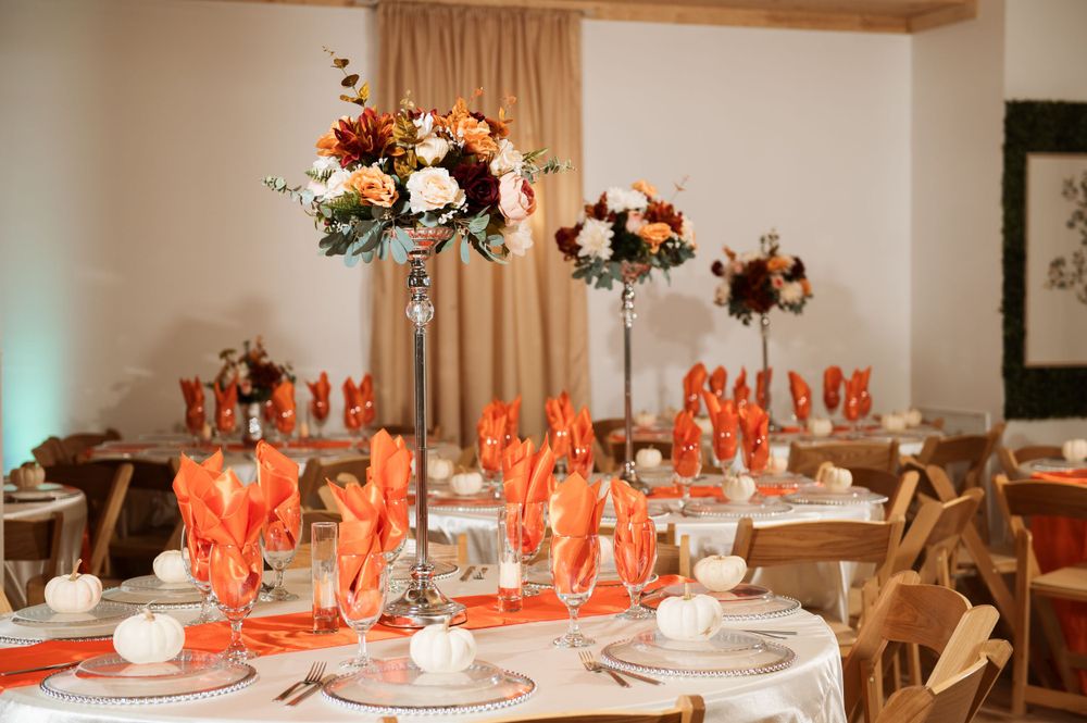 Wedding reception tables decorated with tall floral centerpieces in coral and white with matching napkins.