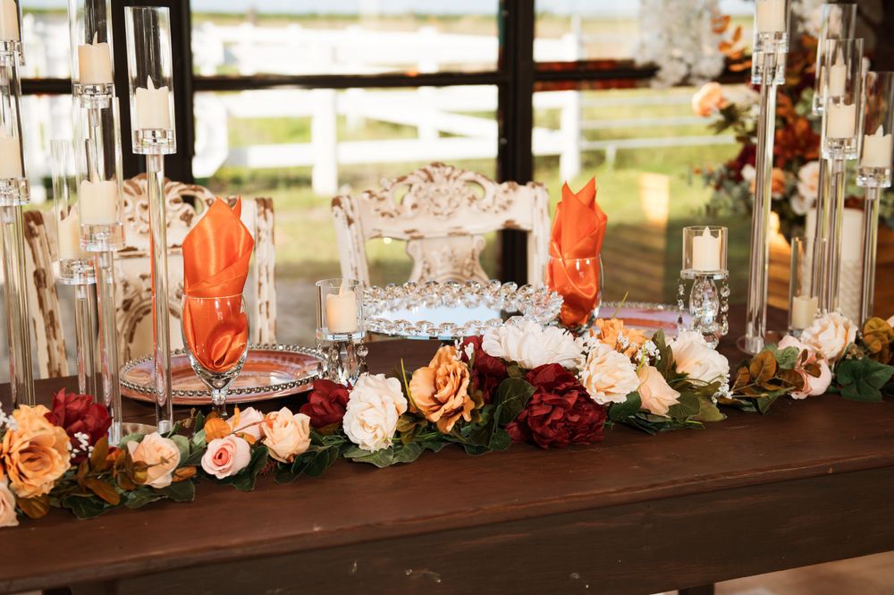 Rustic wood table decorated with orange and burgundy floral arrangements and crystal glassware.