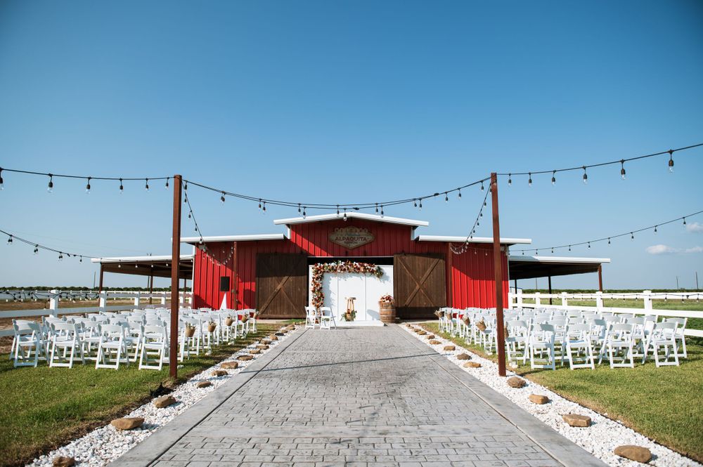 Red barn wedding venue with string lights and white ceremony chairs leading to the entrance.