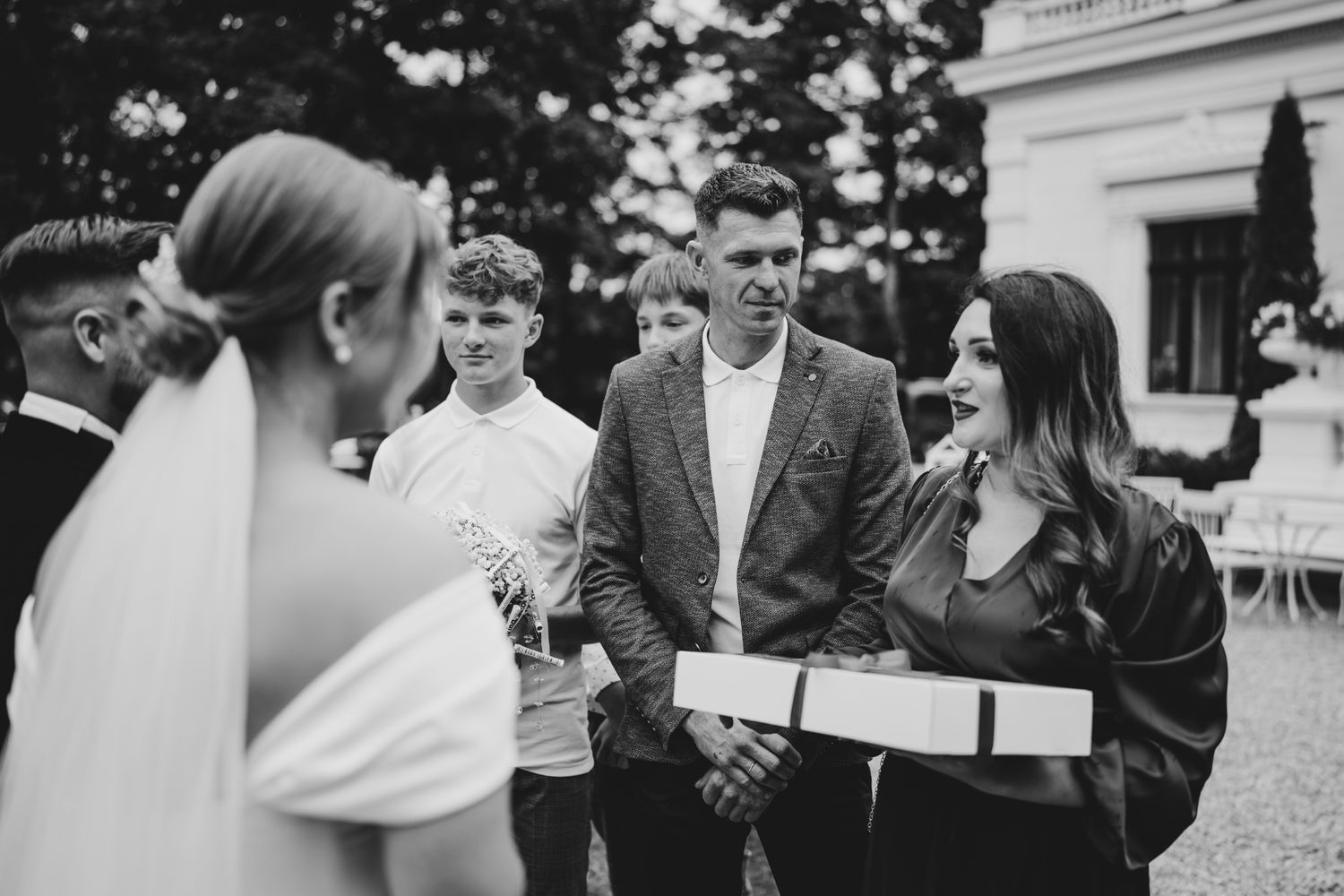 Outdoor wedding reception with guests gathered near a classic white building.
