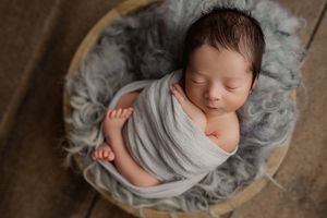 Newborn baby sleeping peacefully on soft gray fur blanket in professional studio setting.
