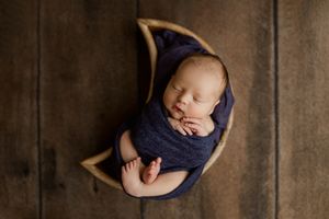 A sleeping newborn baby wearing a navy blue wrap is photographed from different angles in a dark rustic setting.