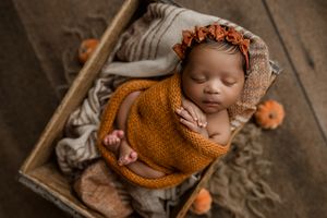Sleeping baby in autumn-themed setting with orange and brown decor and knit sweater on rustic wooden backdrop.
