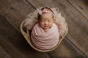 Seven sequential photos show a sleeping newborn in pink swaddle blankets posed on rustic wooden flooring.
