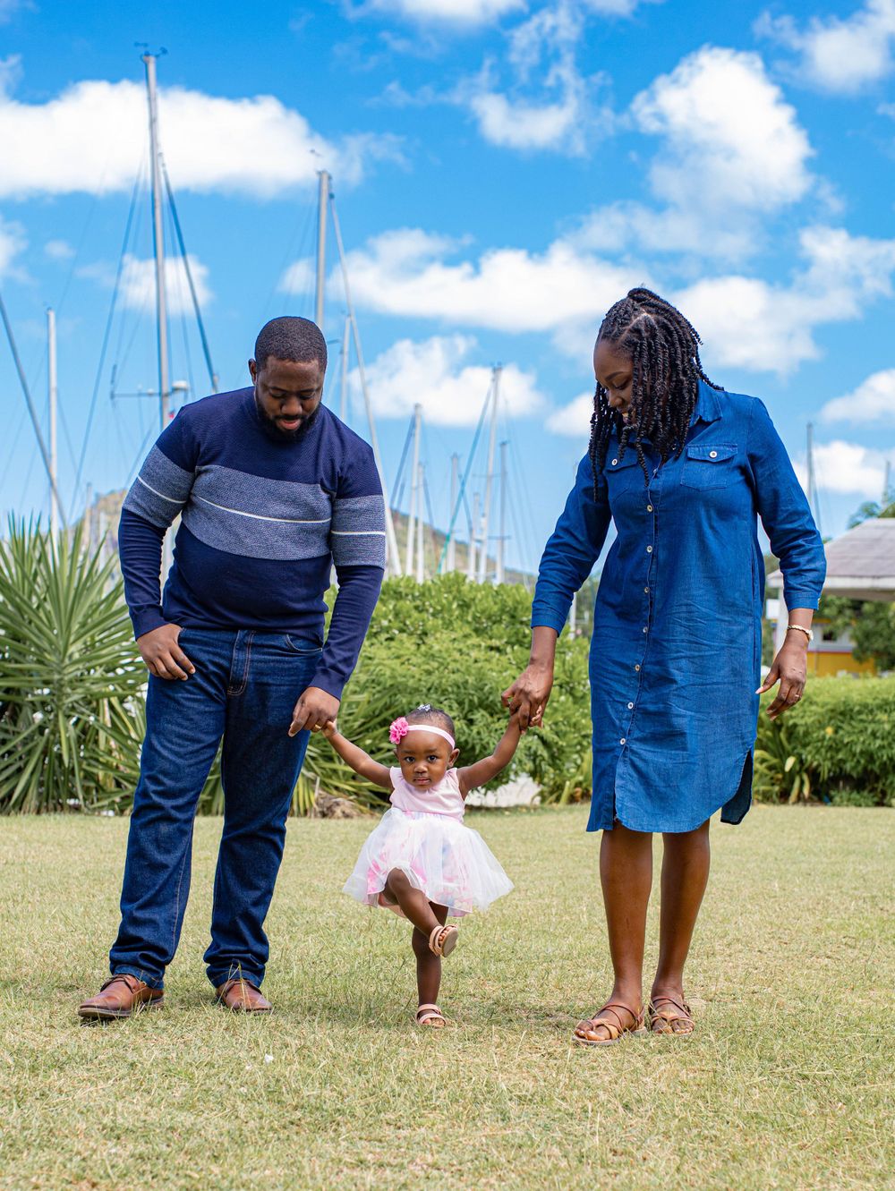 A joyful family moment outdoors with sailboats in the background as a toddler in pink dances between parents.