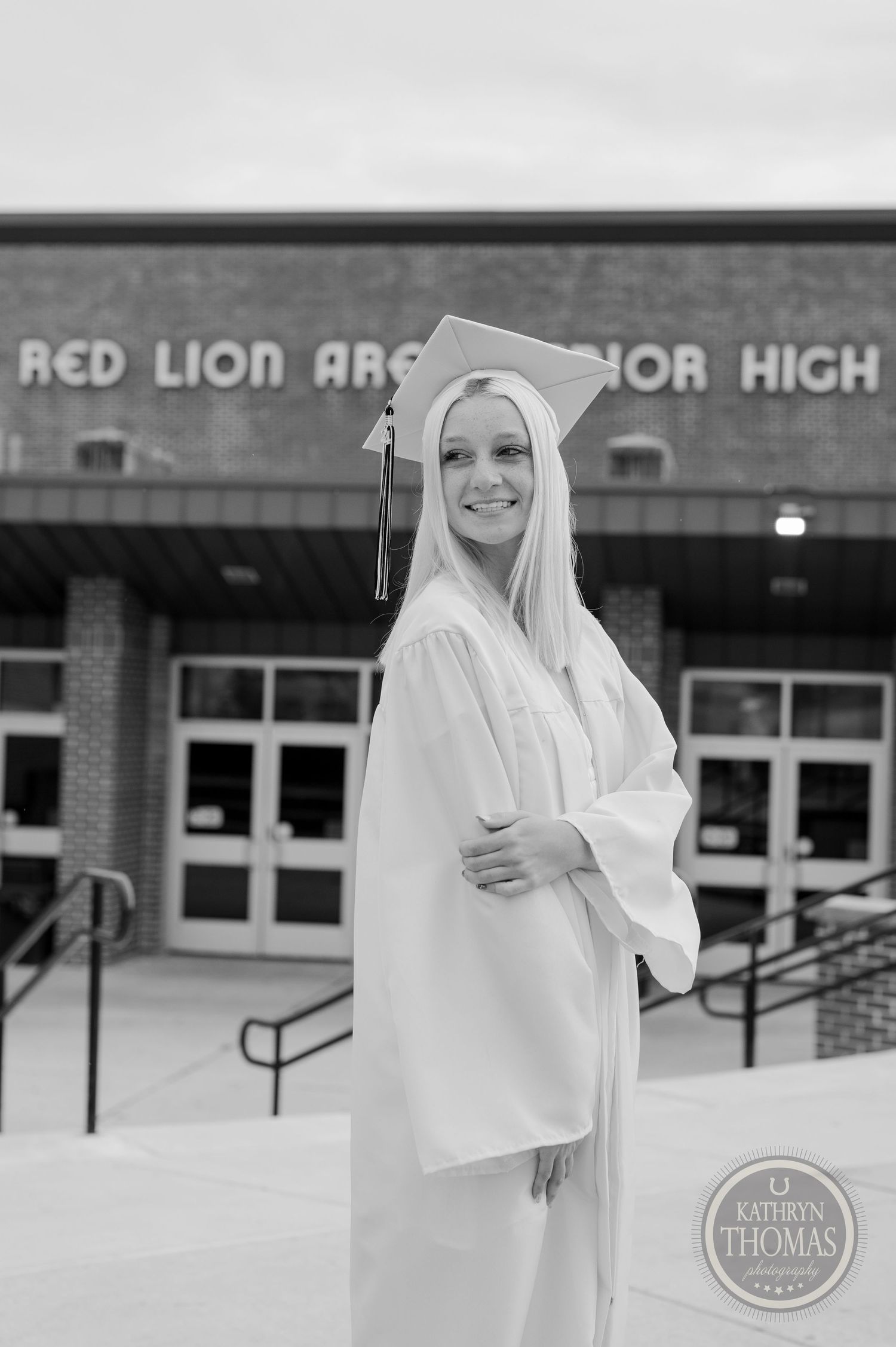 Black and white portrait of graduate in cap and gown outside school building.