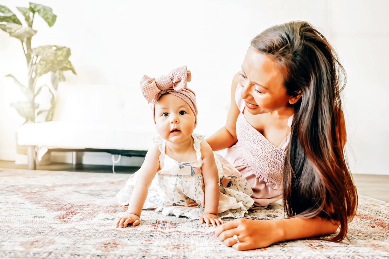 Sweet candid moment of parent and baby in matching pink outfits relaxing on carpet.