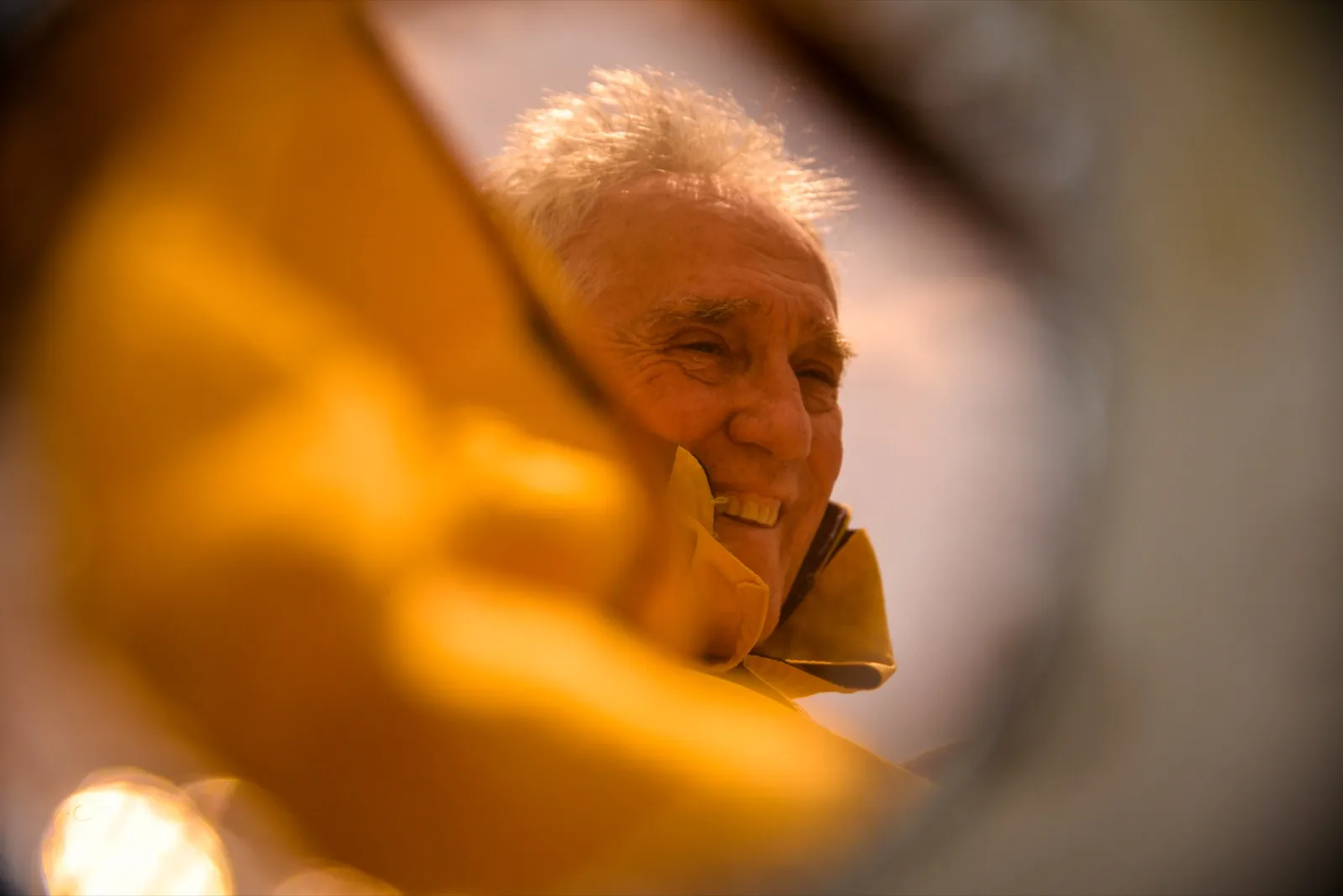 Portrait d’un marin âgé au regard contemplatif, partiellement cadré à travers un ciré jaune.