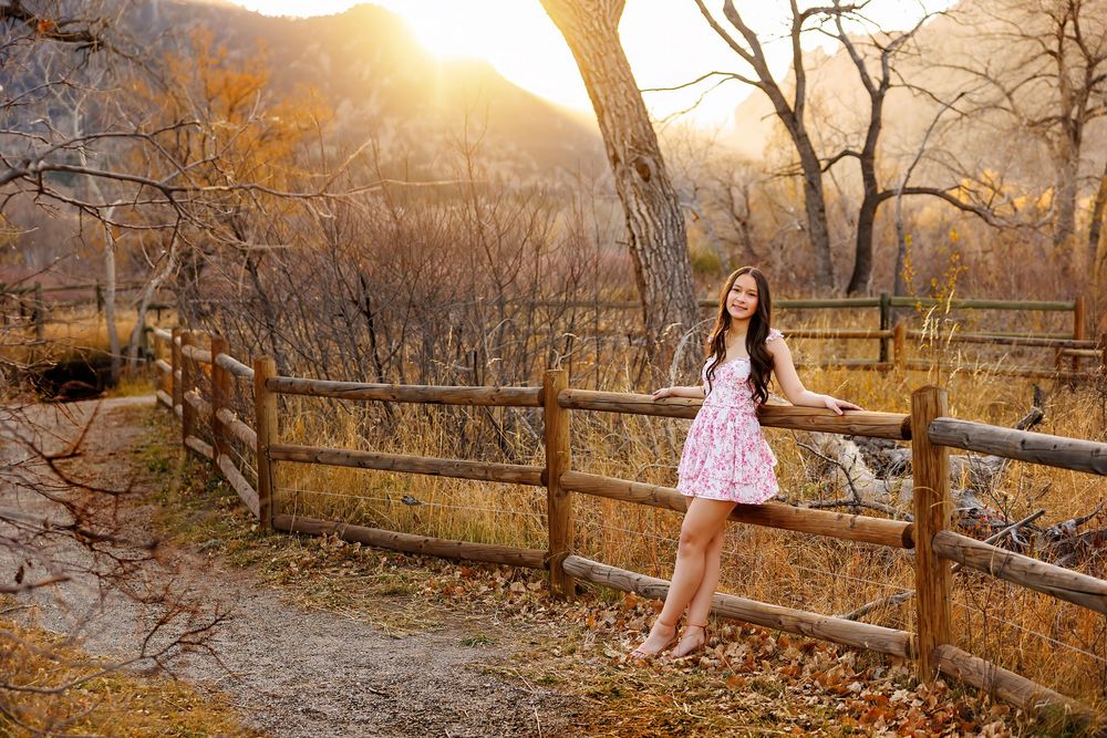 A pink dress against a rustic wooden fence at sunset in an autumn mountain landscape.