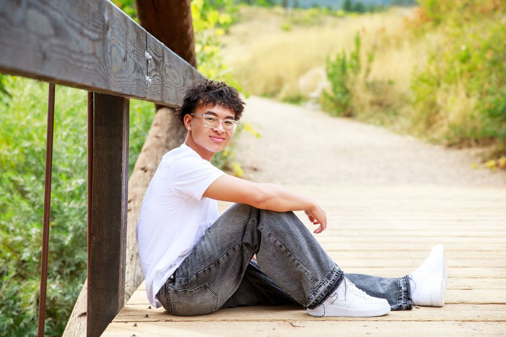 A person sits casually on a wooden deck overlooking a scenic dirt path on a sunny afternoon.