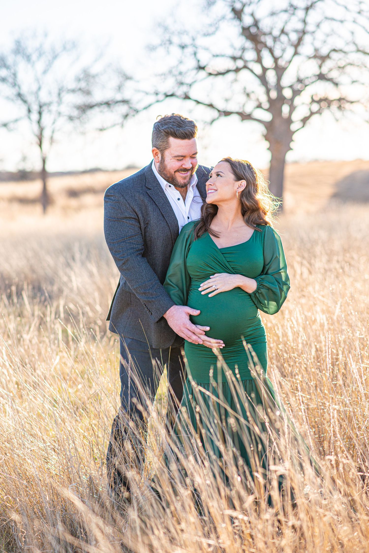 Expectant couple embracing in golden field at sunset.