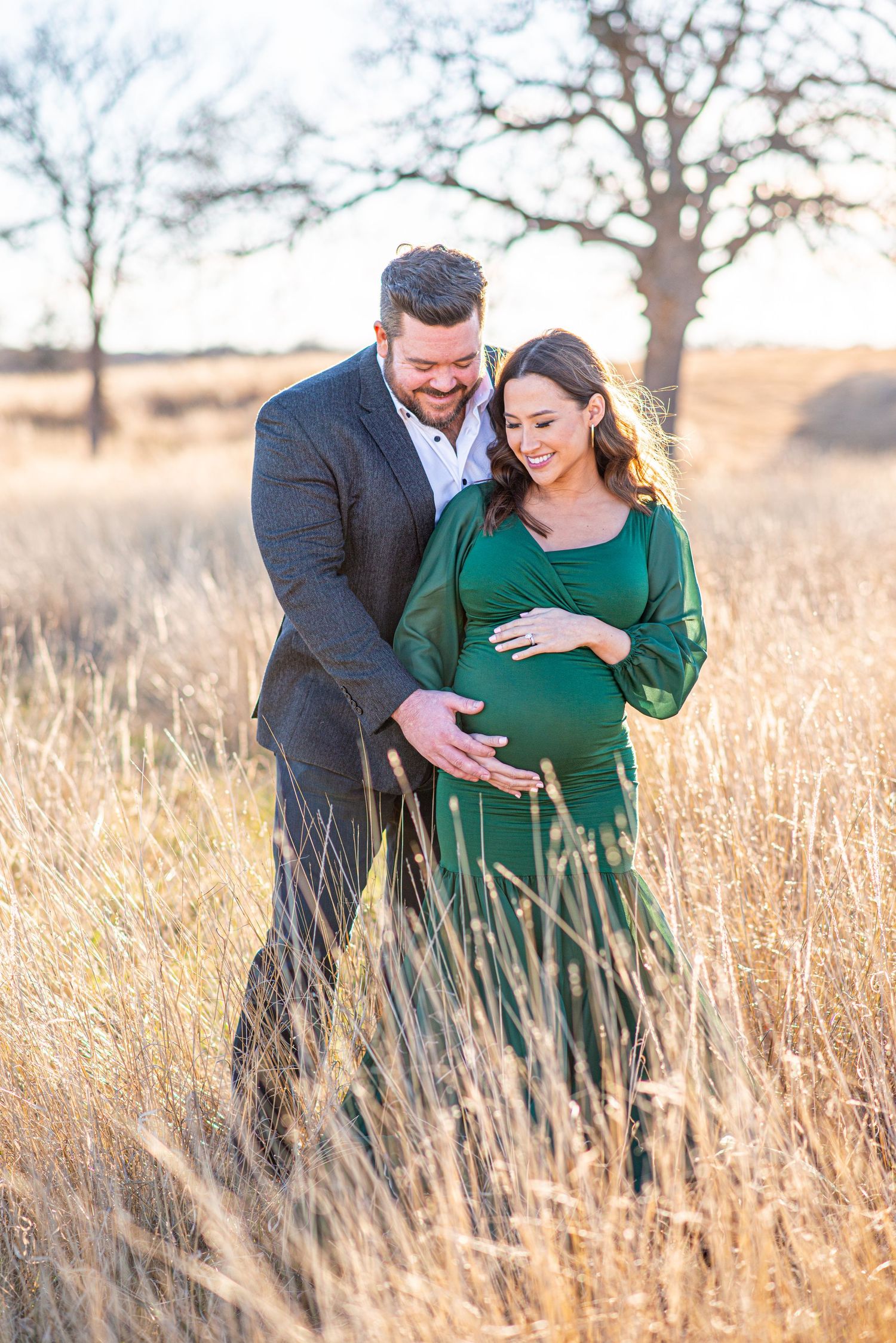 Couple sharing intimate moment in tall prairie grass during maternity photoshoot.