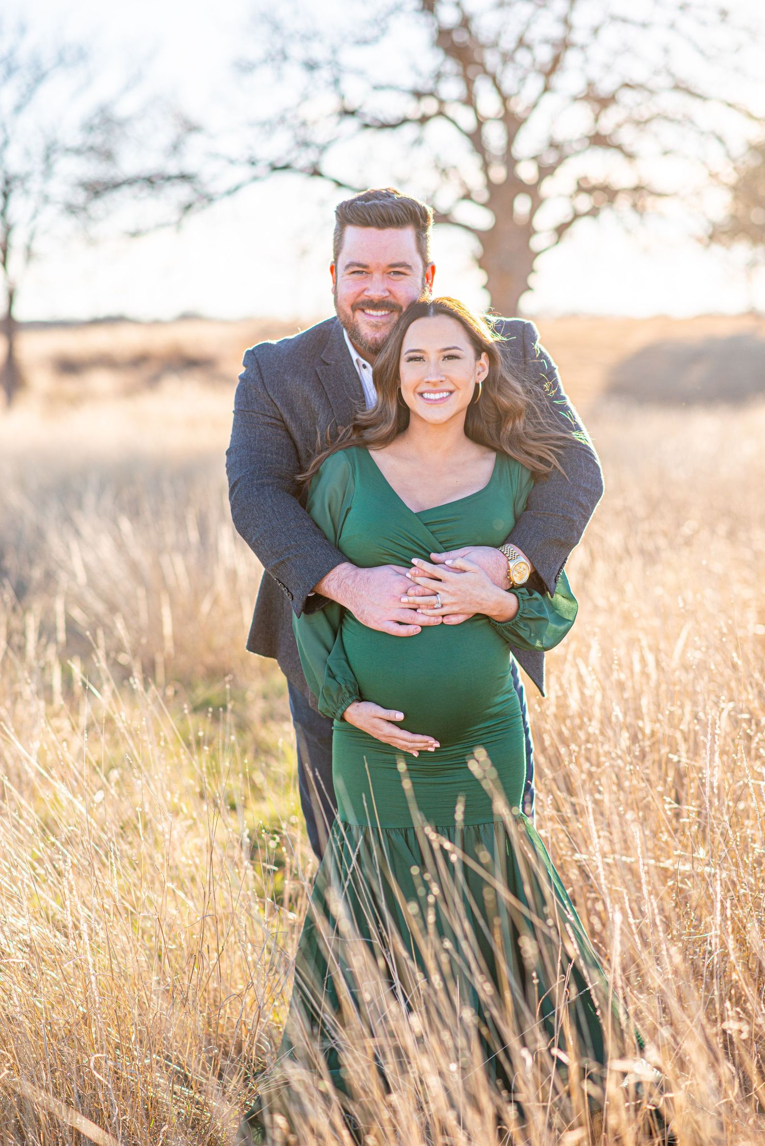 Joyful maternity portrait of couple embracing in sunlit field.