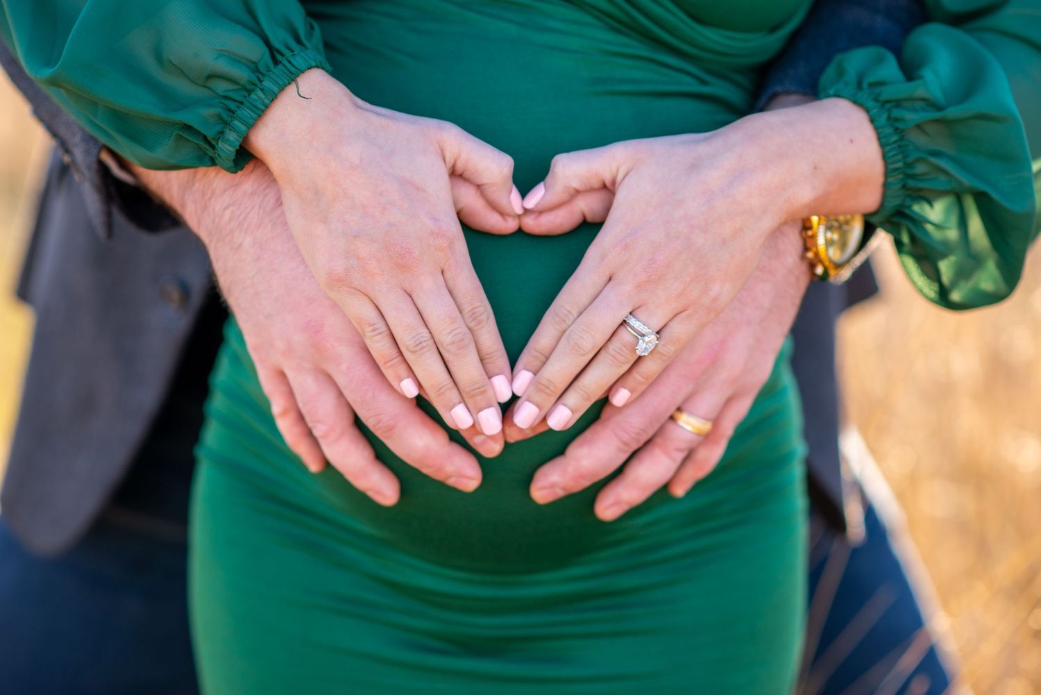 Close-up of hands forming heart shape on green maternity dress.