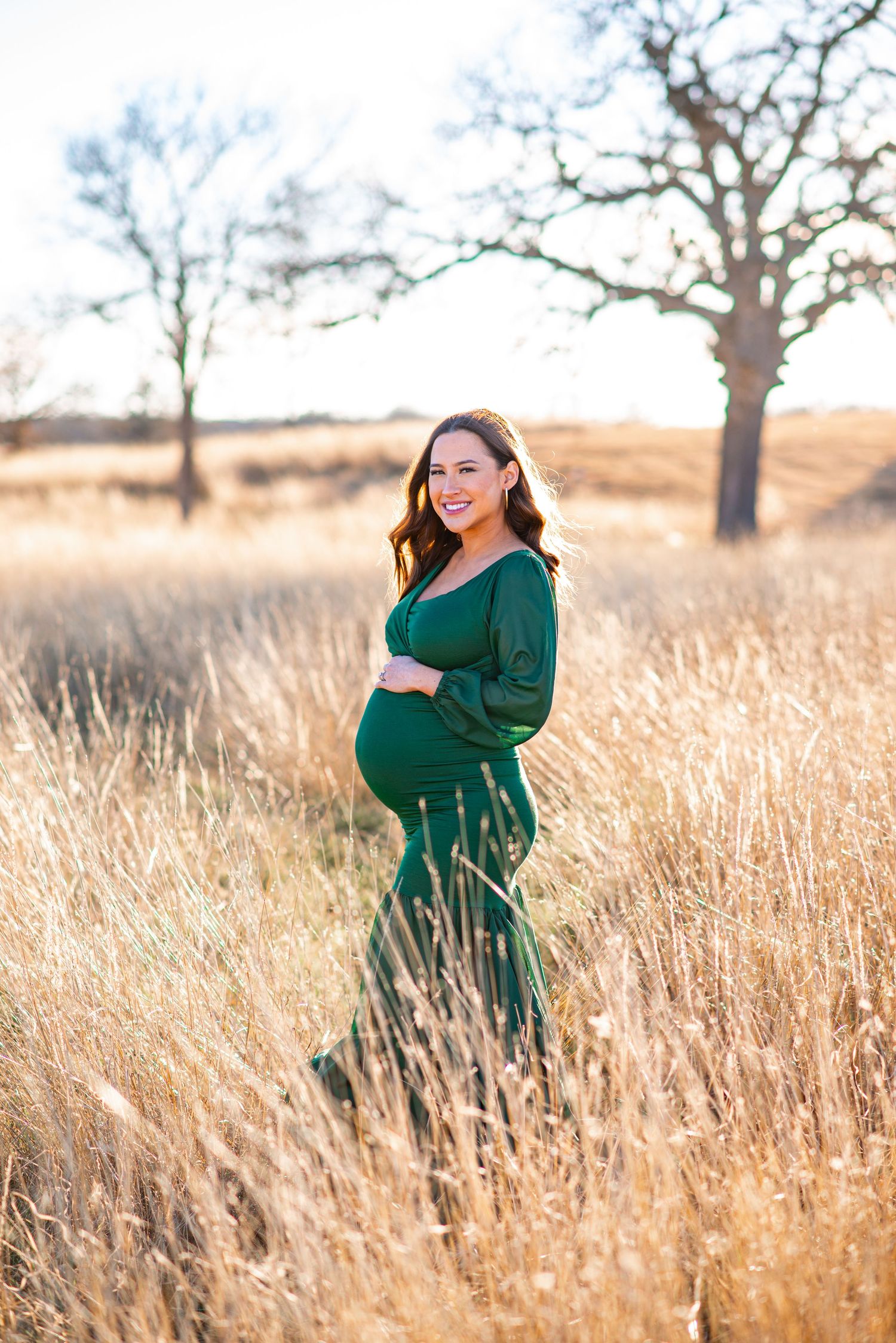 Beautiful pregnancy portrait taken in a sunlit field with tall dry grass and trees.