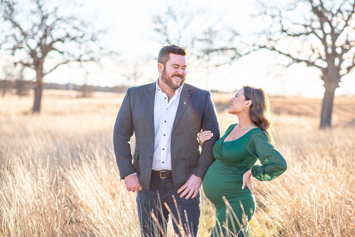 Happy couple laughing together during outdoor maternity session in rustic field setting.