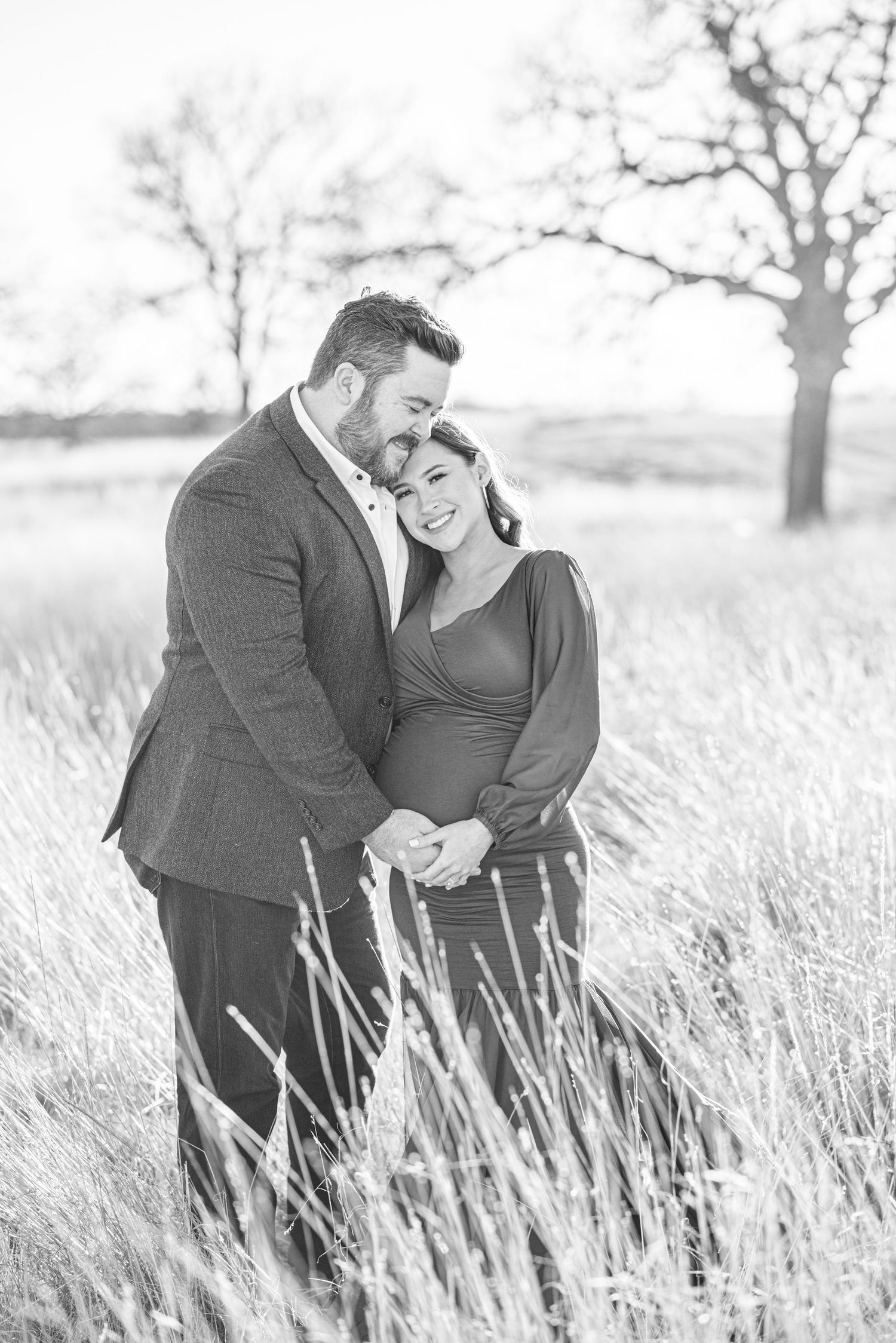 Black and white intimate maternity portrait of couple embracing in tall grass field.