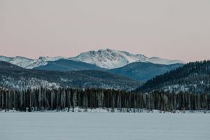 Pine trees, rolling hills, and snowy mountain peaks compressed into a single frame, shot from a great distance on a telephoto lens.