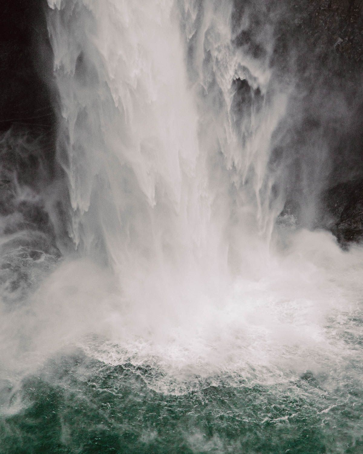 A closeup of the base of Snoqualmie Falls where the falling water hits the river and throws mist and fog in a turbulent storm.