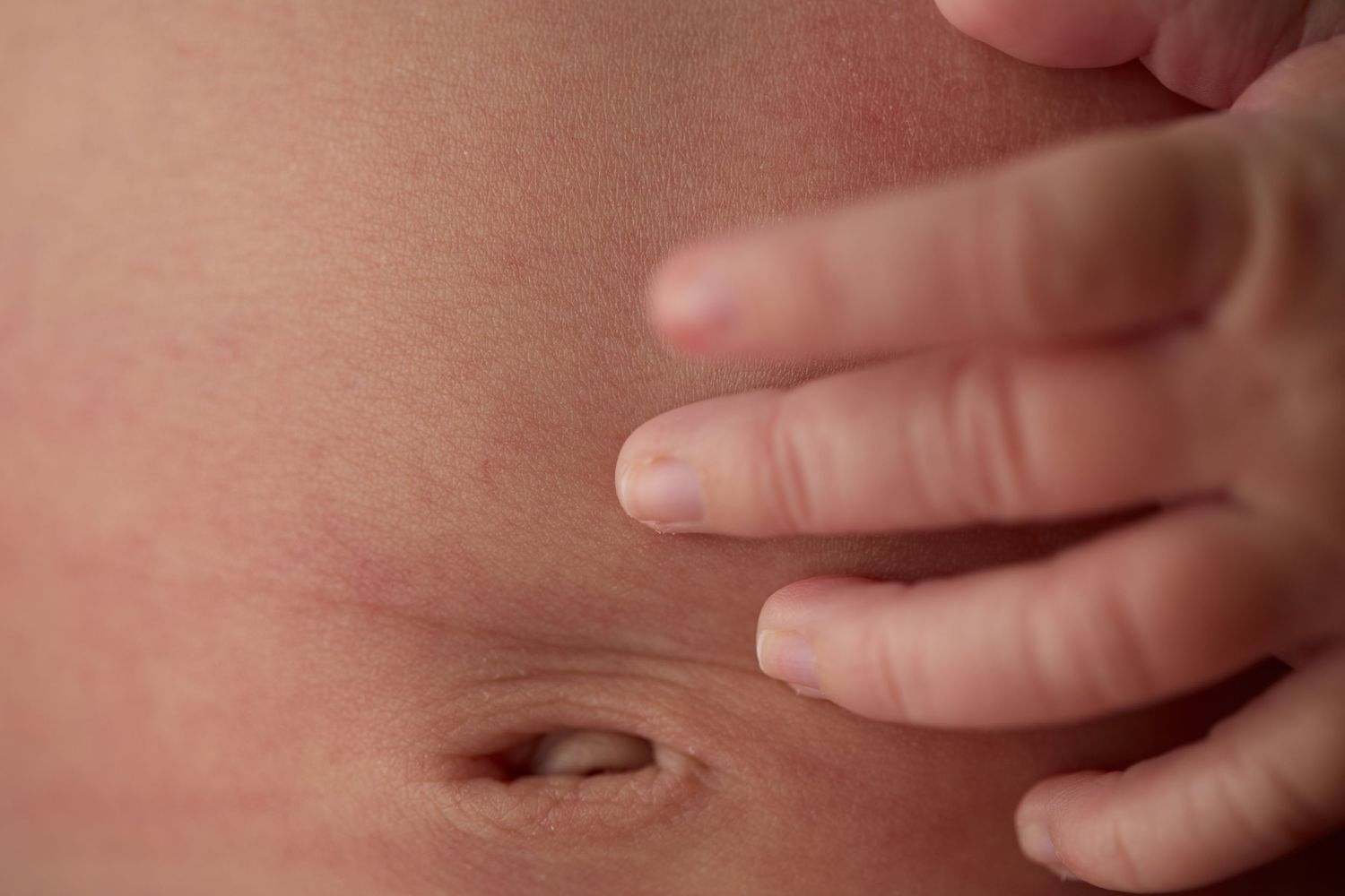 Hand pointing at a belly button on a bare stomach with soft pink skin tones.