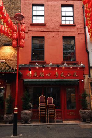 A bright red Chinese restaurant building with traditional red lanterns and stacked chairs in London's Chinatown district.