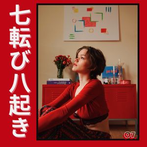 Artistic portrait photo with red theme featuring person in crimson sweater against warm interior with artwork and flowers.