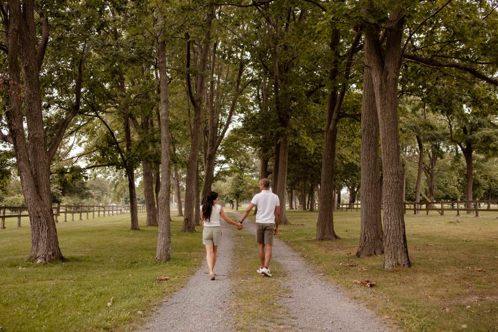 Couple walk the trails of Lake Ontario Park amongst the tall trees and greenspace in Kingston, Ontario, Canada.
