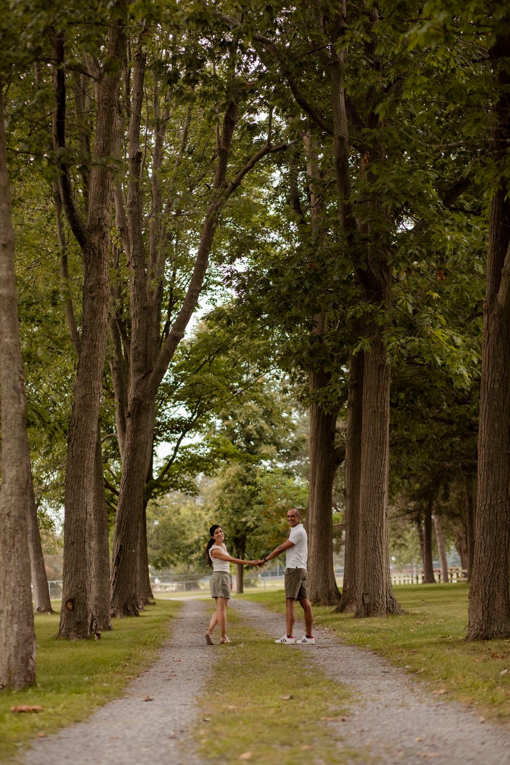 Couple walk the trails of Lake Ontario Park amongst the tall trees and greenspace in Kingston, Ontario, Canada.