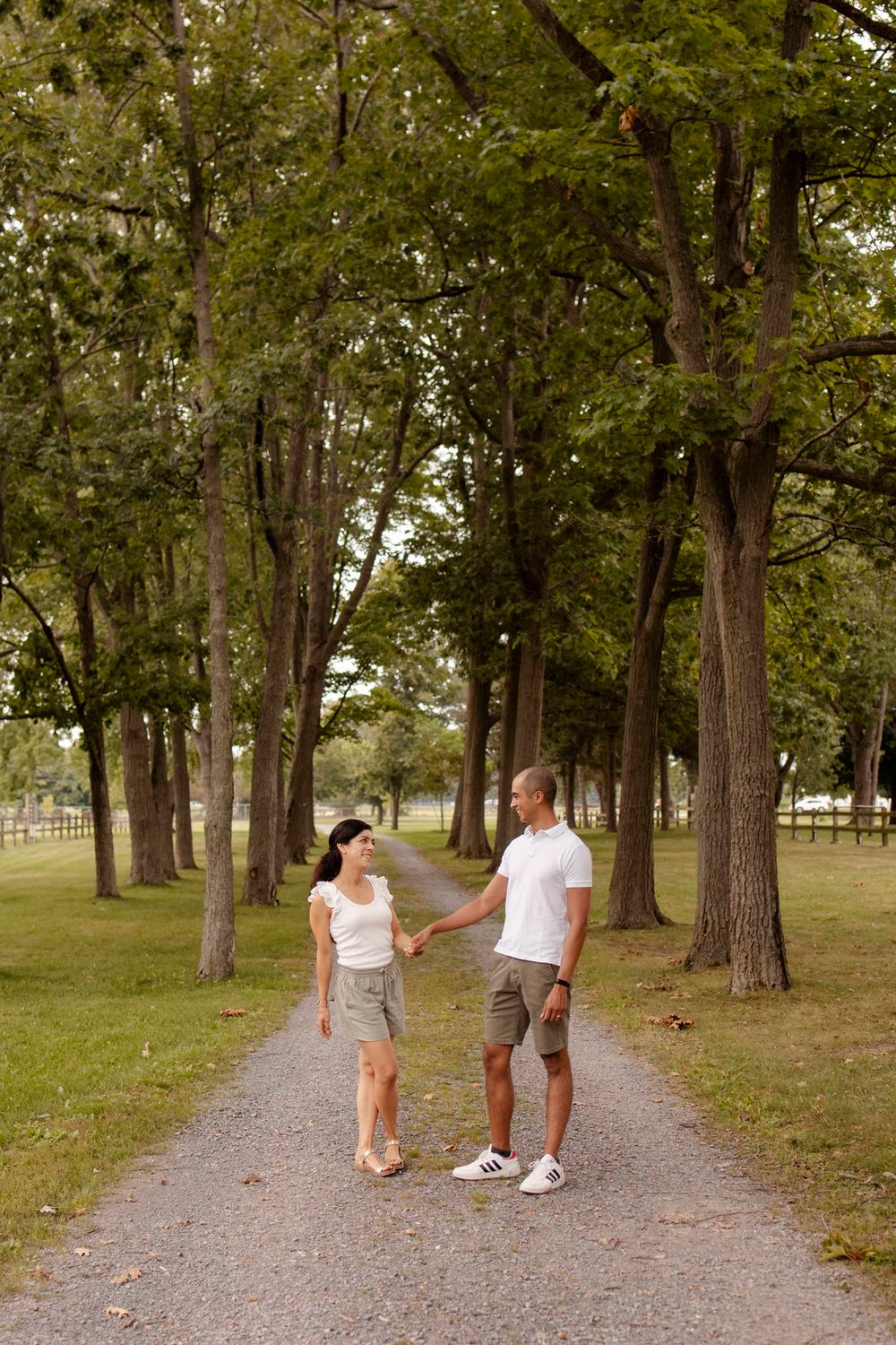 Couple walk the trails of Lake Ontario Park amongst the tall trees and greenspace in Kingston, Ontario, Canada.