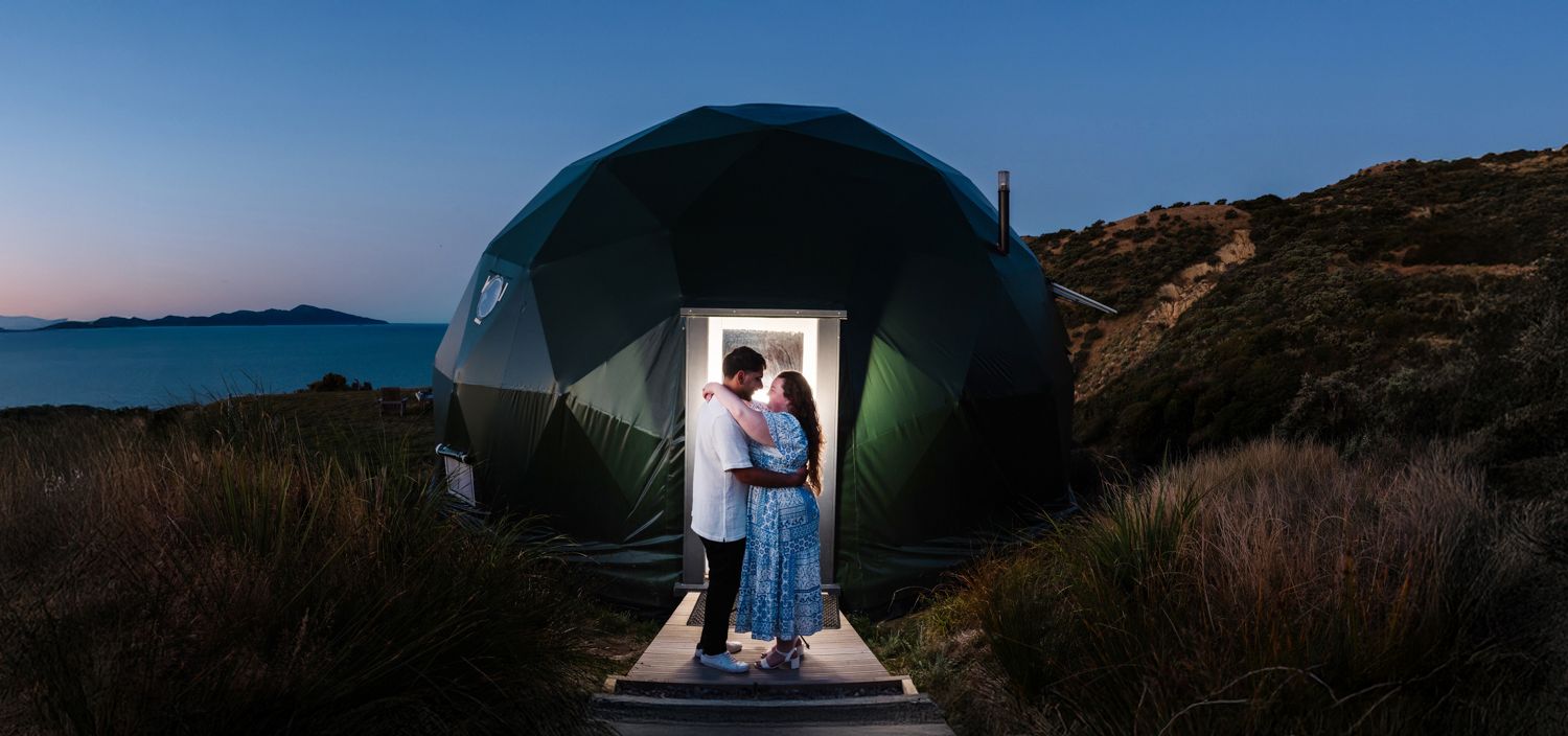Couple hugging at sunset at The Escarpment Domes with Kapiti Island in the background