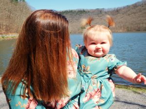 A pair wearing coordinating teal floral dresses sit together by a scenic lake.