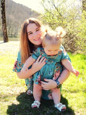 Two people in matching teal floral dresses share a sunny outdoor moment together.