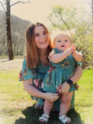Two people share joyful smiles while wearing matching teal floral dresses outdoors.