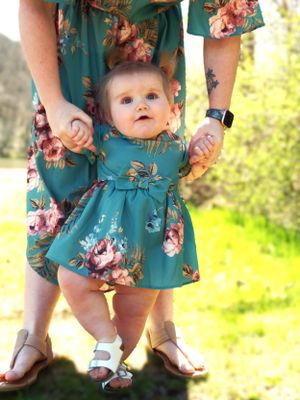 Close-up of matching teal floral dresses and white sandals in a sunny outdoor setting.