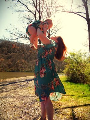 A sunlit moment of playful lifting by a lakeside with trees in the background.